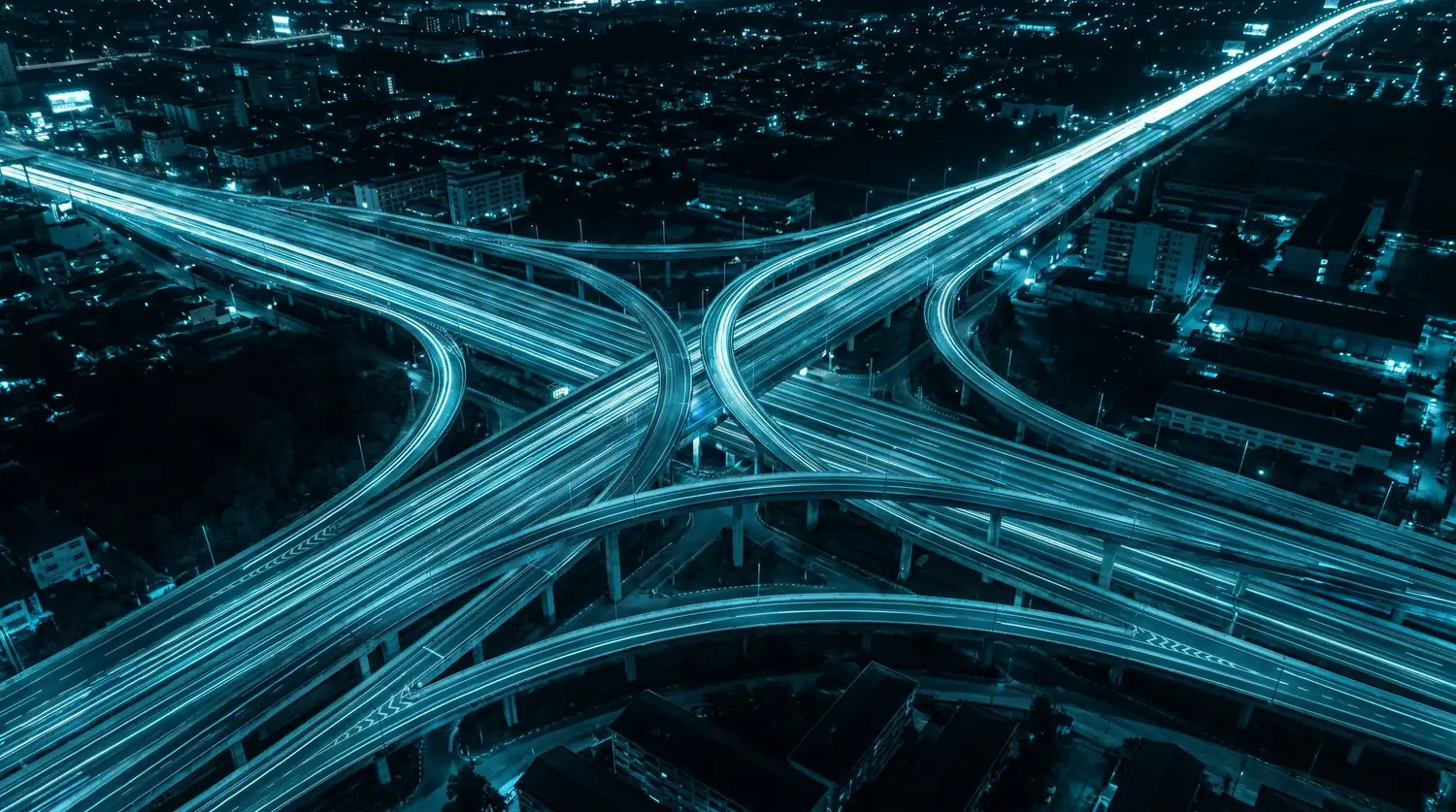 Entroncamento rodoviário à noite, com os rastros de luz dos veículos